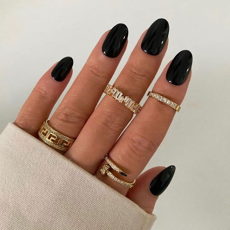 Mão de pele clara, com anéis em dourado e unha amendoada preta Like Magazine