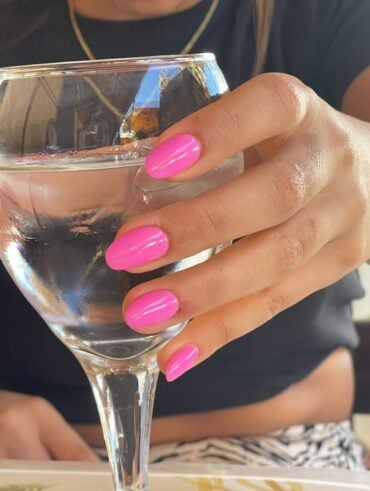 Mão de pele clara, segurando uma taça, com unha amendoada rosa-chiclete