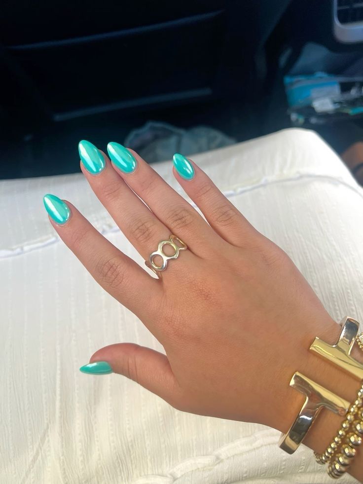 Mão de pele clara, com acessórios em dourado e unha amendoada verde-água