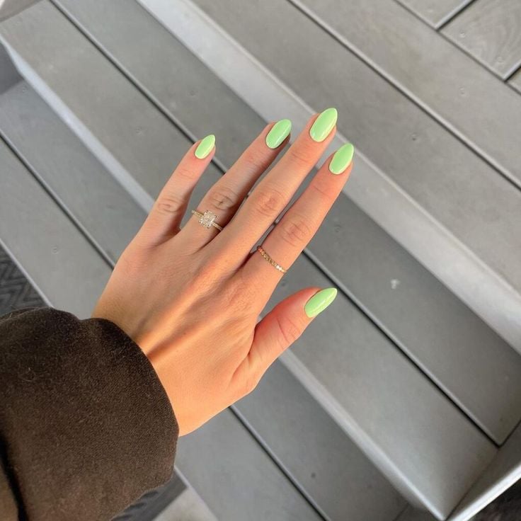Mão de pele clara, com anéis em dourado e unha amendoada verde-claro