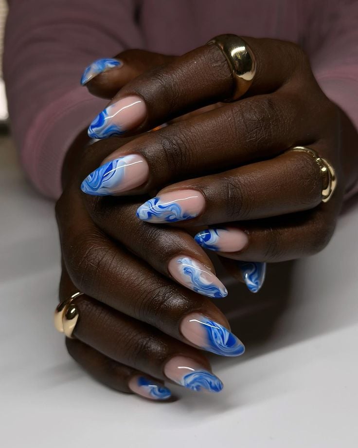 Mãos de pele preta, com anéis em dourado e unha amendoada azul decorada