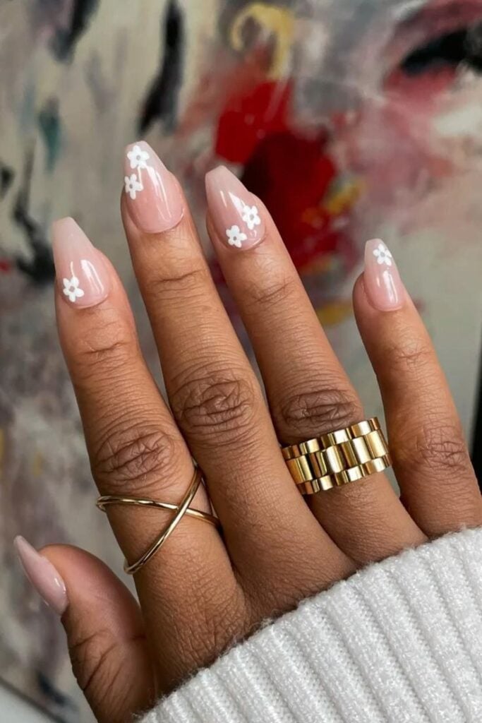 Mão de pele média, com anéis em dourado e unha bailarina com flores brancas