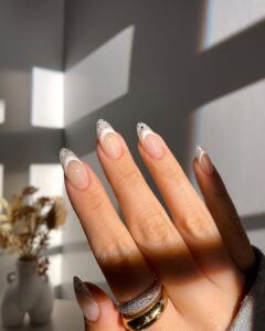 Mão de pele clara, com anéis em dourado e unha amendoada com francesinha branca com glitter prata
