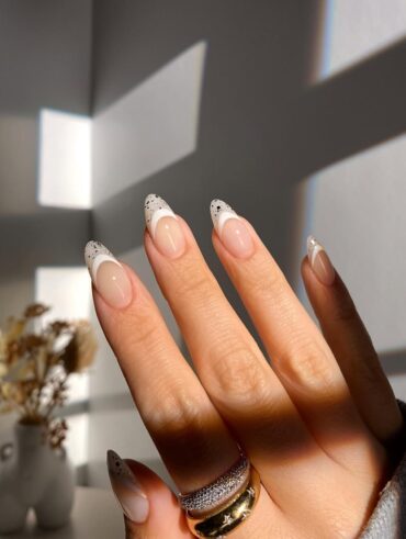 Mão de pele clara, com anéis em dourado e unha amendoada com francesinha branca com glitter prata