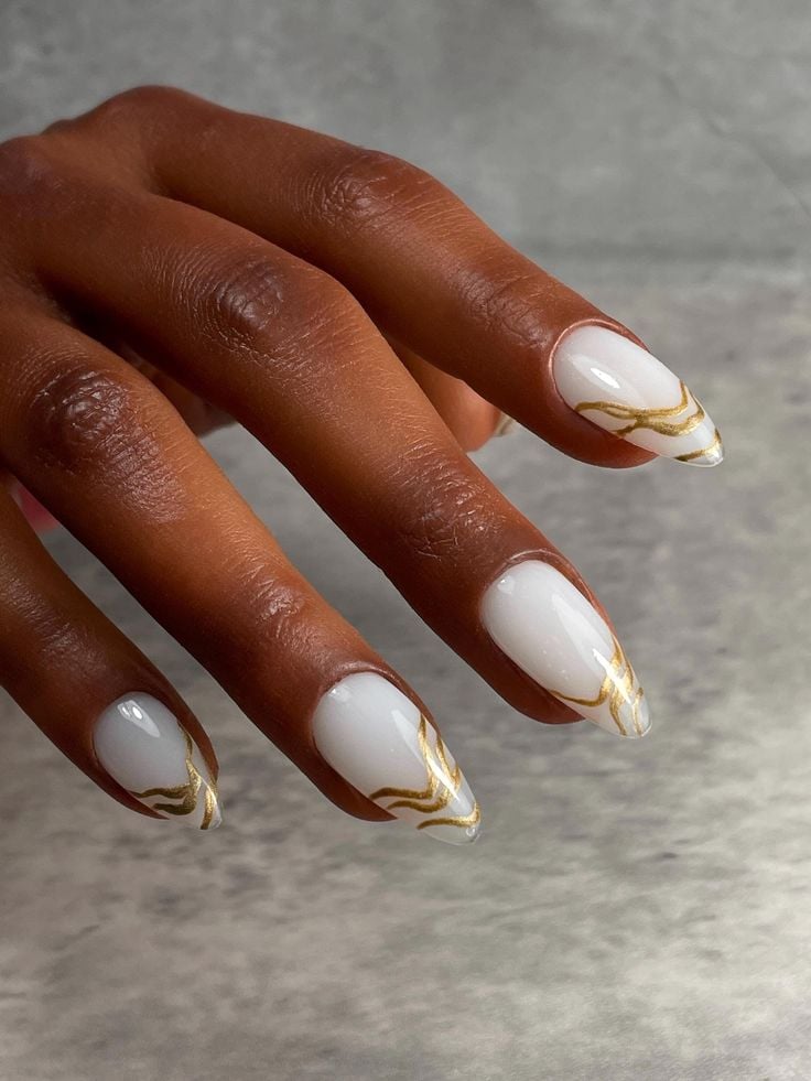 Mão de pele preta, com unha amendoada branca com linhas fluidas em dourado