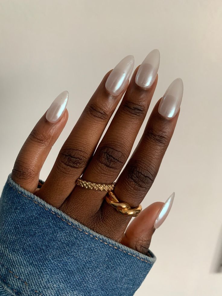Mão de pele preta, com acessórios em dourado e unha amendoada branca perolada