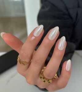 Mão de pele clara, com acessórios em dourado e unha amendoada clara e perolada