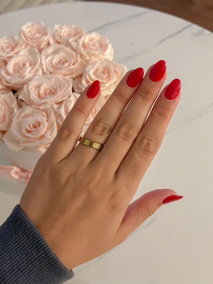 Mão de pele clara, com anel em dourado e unha amendoada com esmalte vermelho-alaranjado