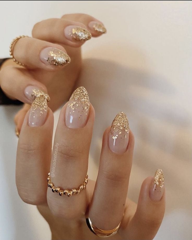 Mãos de pele clara, com anéis em dourado e unha com glitter dourado
