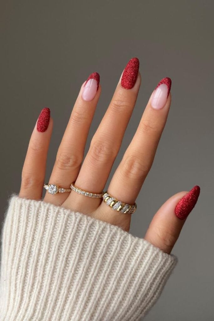 Mão de pele clara, com acessórios brilhosos em dourado, e unha amendoada vermelha e com francesinha vermelha de glitter 