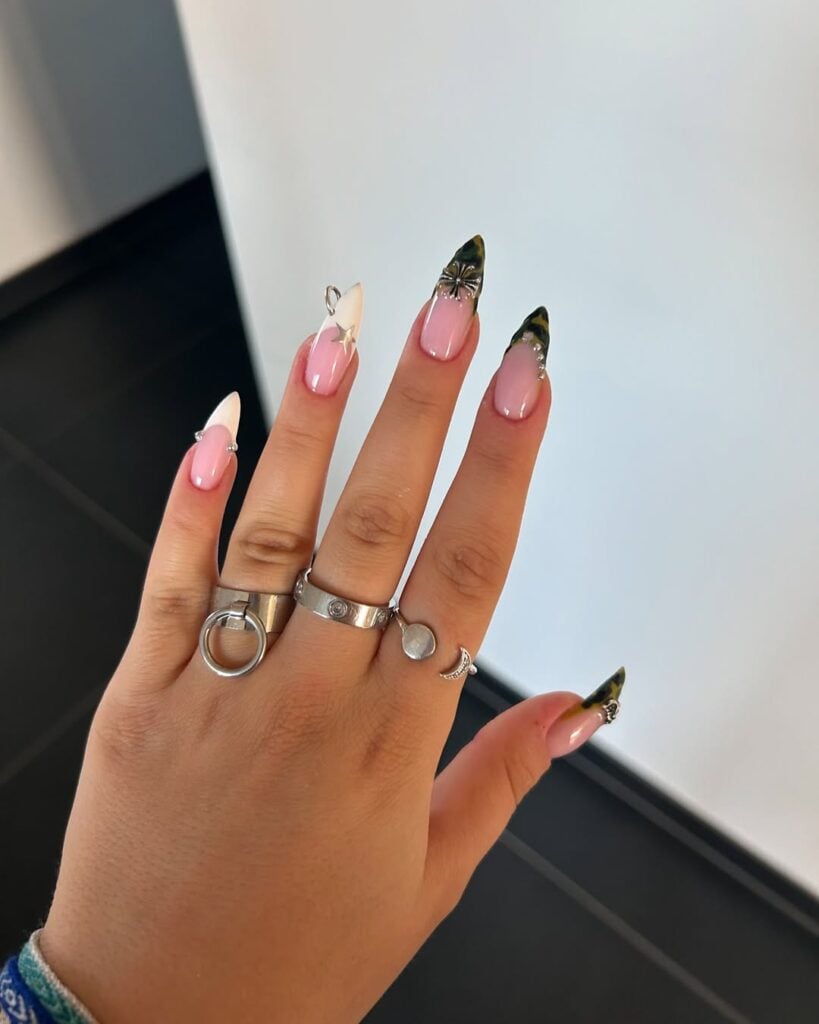 Mão de pele clara, com acessórios em prata e unha stiletto com francesinha e piercing
