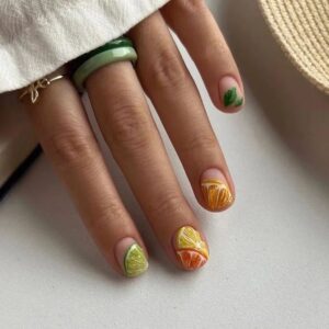 Mão de pele clara, com anel dourado e colorido e unhas curtinhas com 'estampa' de fruta