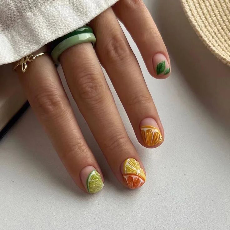 Mão de pele clara, com anel dourado e colorido e unhas curtinhas com 'estampa' de fruta