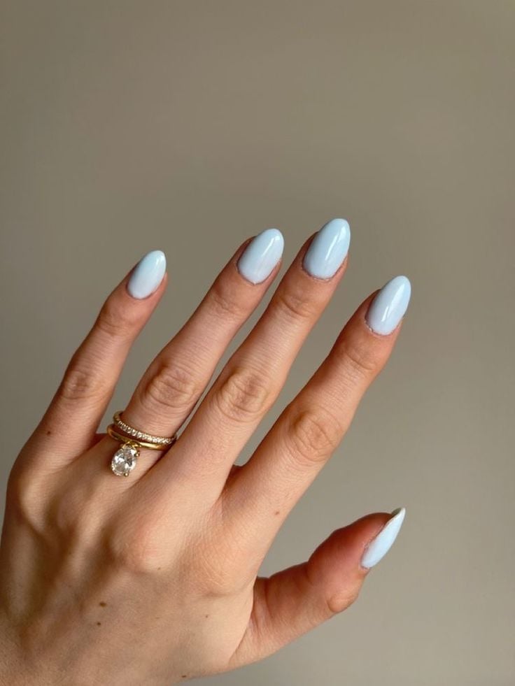 Mão de pele branca, com anéis em dourado e unha curta e amendoada azul-céu 