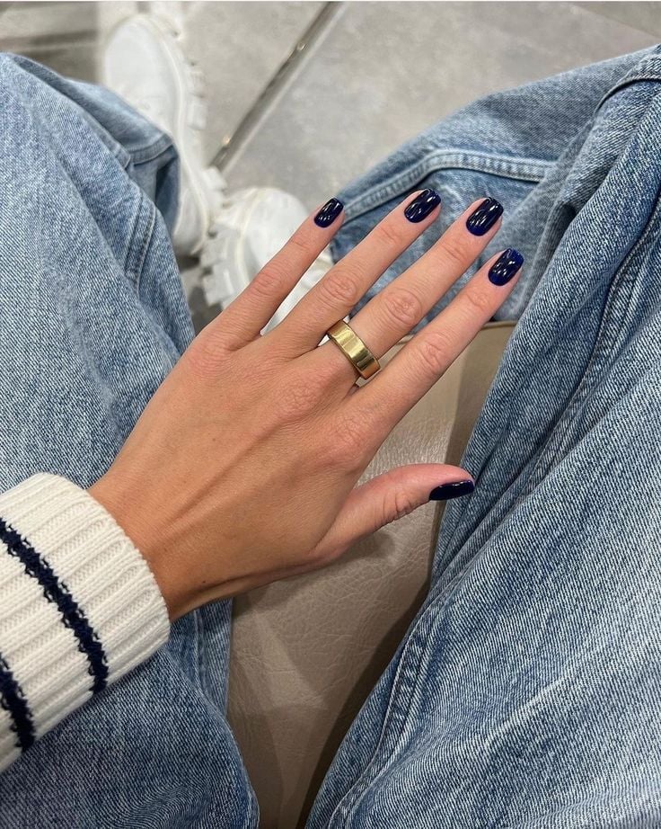Mão de pele branca, com anel em dourado e unha curta e quadrada azul-marinho