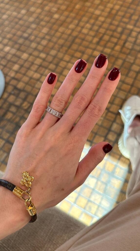 Mão de pele branca, com acessórios em dourado e prata e unha curta e quadrada cereja