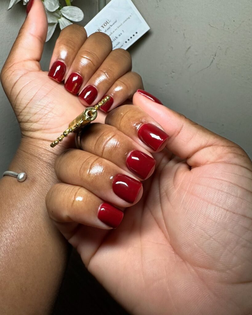 Mãos de pele preta, com acessórios em dourado e unha curta e quadrada vermelho-cereja 