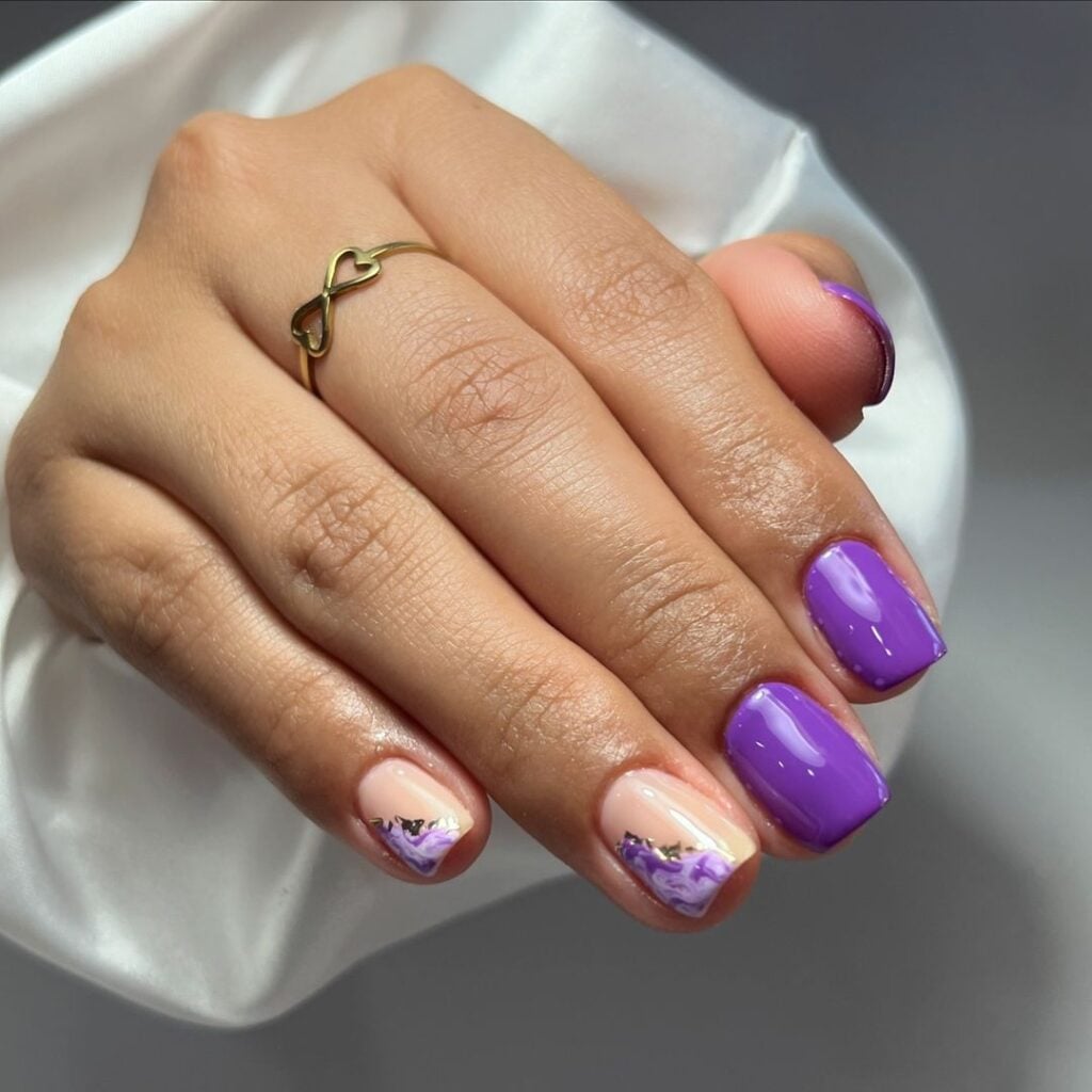 Mão de pele branca, com anel em dourado e unha curta e quadrada violeta 
