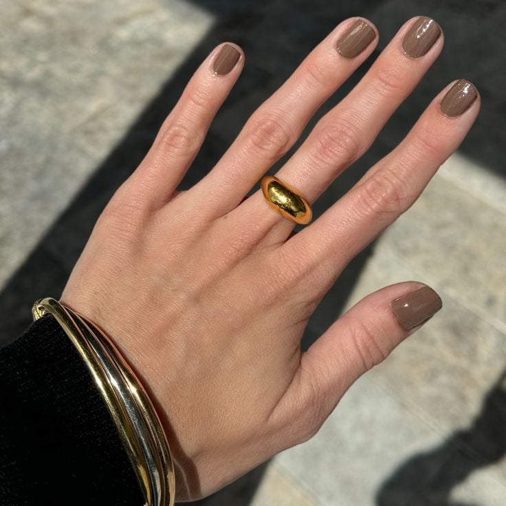 Mão de pele branca, com anel em dourado e unha curta mocha mousse