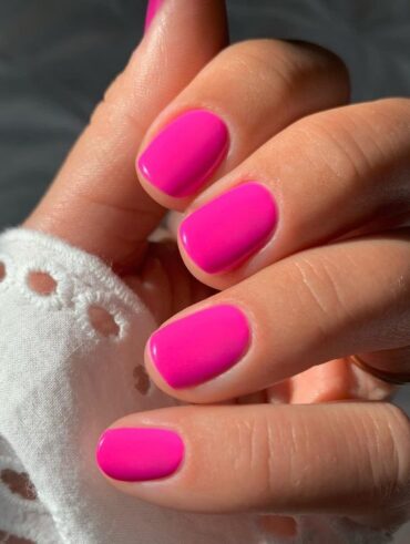 Mão de pele clara, com unha curtinha rosa neon