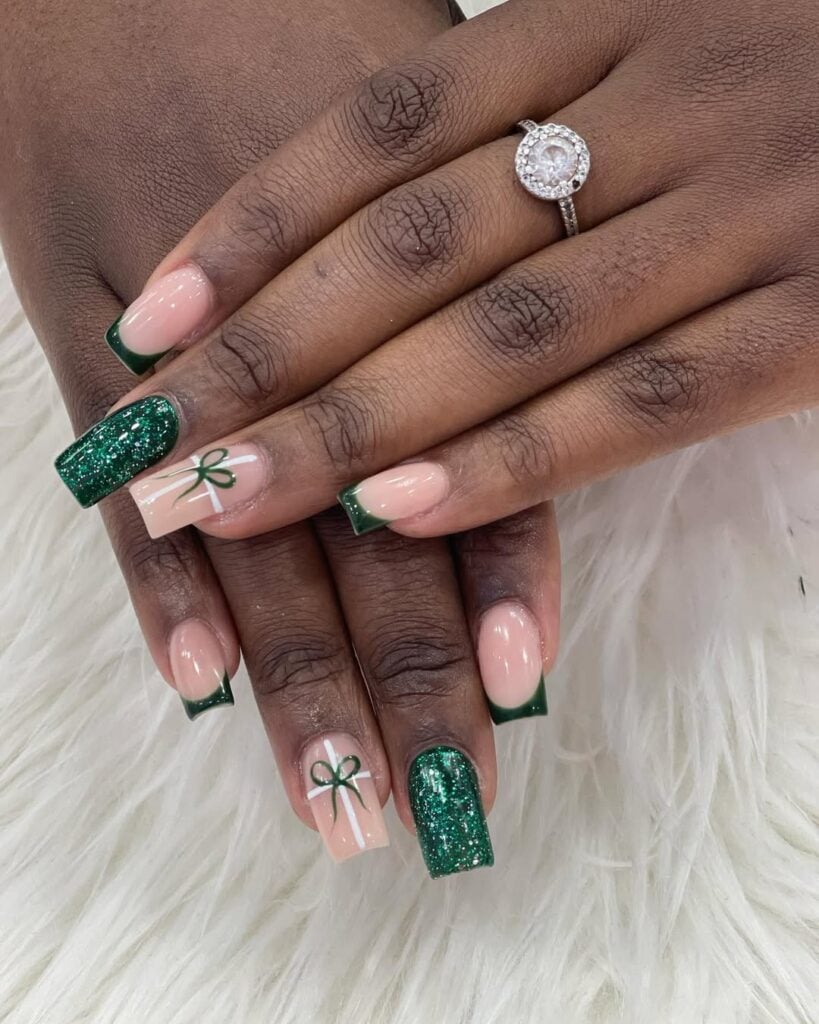 Mãos de pele preta, com acessórios em prata e unha quadrada nude, com decorações em verde com glitter