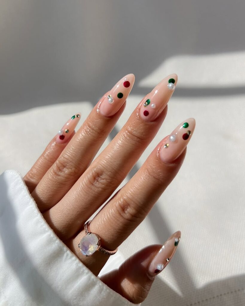 Mão de pele branca, com acessório em dourado e unha amendoada nude com pedrinhas coloridas 