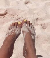 Pés de pele preta, com areia e unha amarelo-manteiga