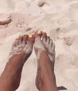 Pés de pele preta, com areia e unha amarelo-manteiga
