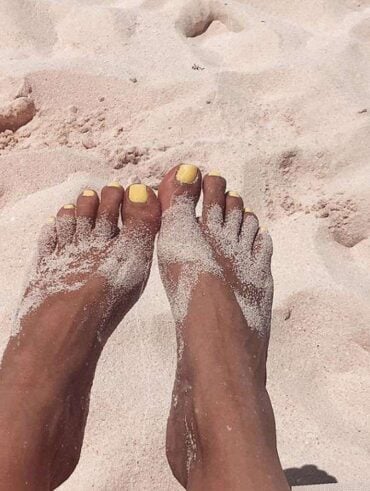 Pés de pele preta, com areia e unha amarelo-manteiga