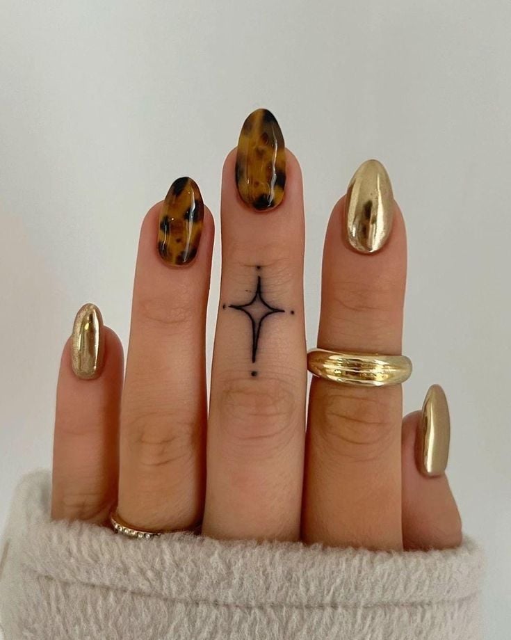 Mão de pele clara, com anéis em dourado e unha amendoada dourada e com estampa de tartaruga