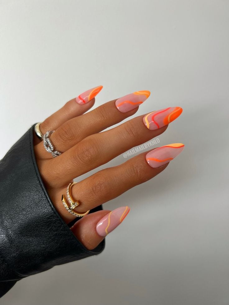 Mão de pele média, com acessórios em prata e dourado e unha amendoada com linhas fluidas em laranja 