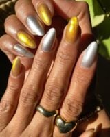 Mãos de pele clara, com anéis em dourado e unha amendoada prata e dourada magnética