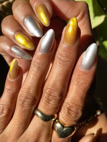 Mãos de pele clara, com anéis em dourado e unha amendoada prata e dourada magnética