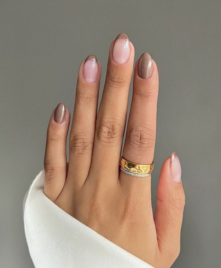 Mão de pele branca, com acessórios em dourado e unha amendoada mocha mousse