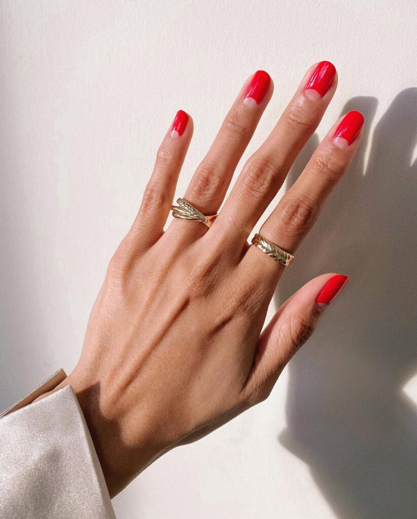 Mão de pele branca, com unha curta e redonda usando esmalte vermelho, com nail art cut out