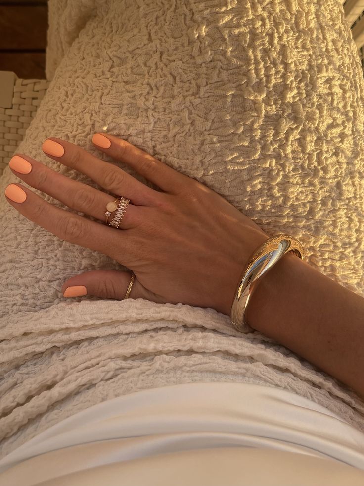 Mão de pele clara-média, com acessórios em dourado e unha pêssego 