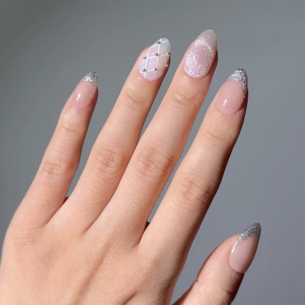 Mão de pele clara, com unha amendoada com francesinha de glitter prata, esmalte magnético prata e 'renda'