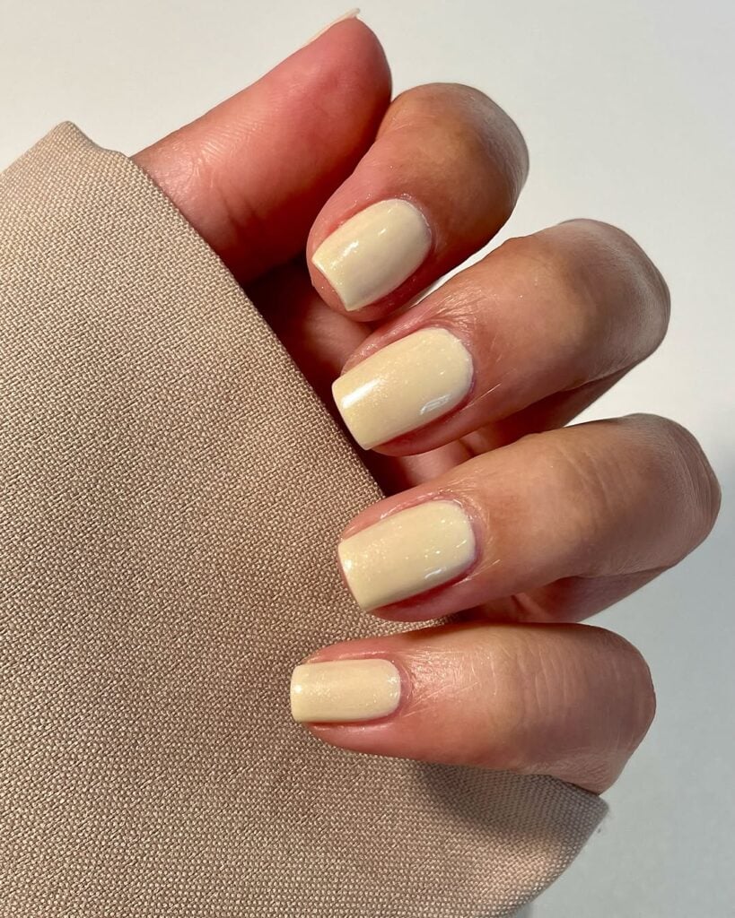 Mão de pele clara, com unha curta e quadrada amarelo-manteiga 