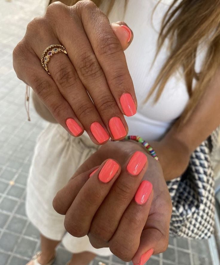 Mãos de pele preta, com acessórios em dourado e unha squoval coral 