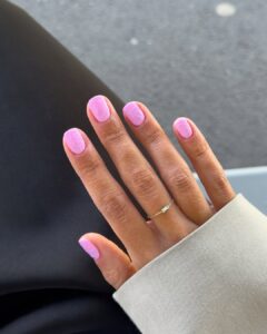 Mão de pele clara, com anel fininho e unha quadrada rosa com linhas fluidas coloridas