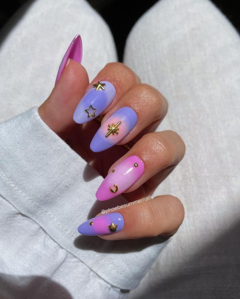 Mão de pele branca, com nail art nas cores rosa e azul com charms de estrelas e lua