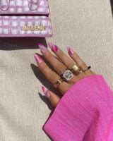 Mão de pele clara, com acessórios em dourado e unha amendoada rosa e roxa