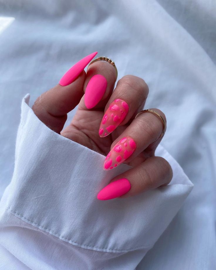 Mão de pele clara, com acessórios em dourado e unha stiletto rosa neon decorada