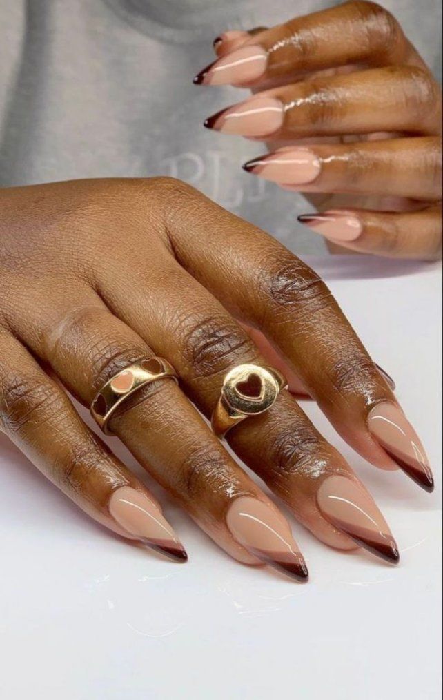 Mãos de pele preta, com acessórios em dourado e unha stiletto nude com decorações em marrom