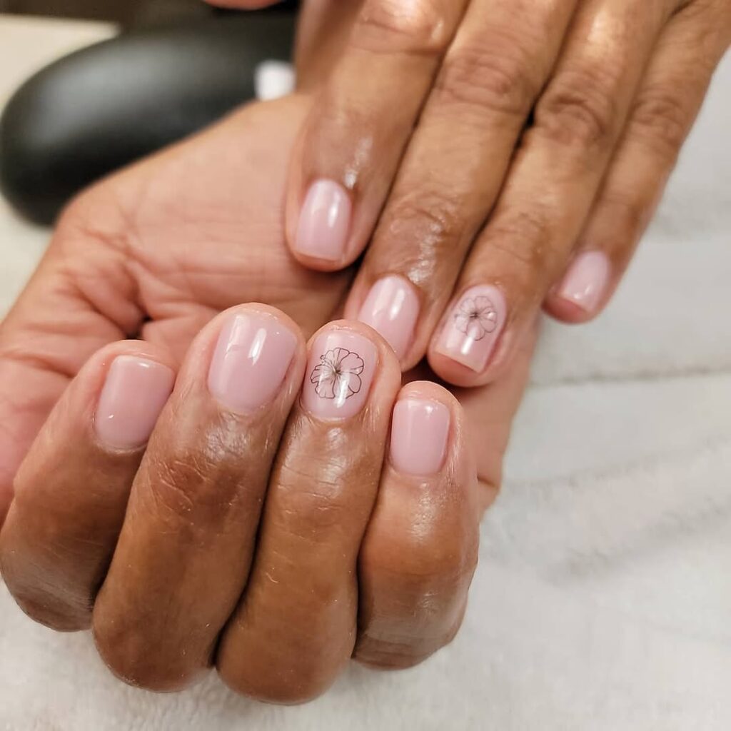 Mãos de pele preta, com unha curta squoval rosa transparente com flor preta
