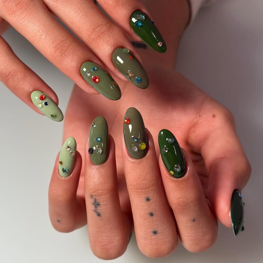 Mãos de pele clara, com unha amendoada verde-escuro e claro e decorada com strass