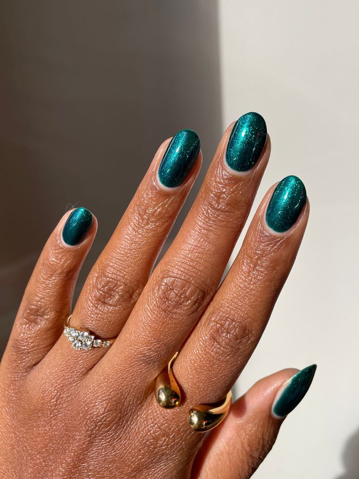 Mão de pele preta, com acessórios em prata e dourado e unha amendoada verde-esmeralda