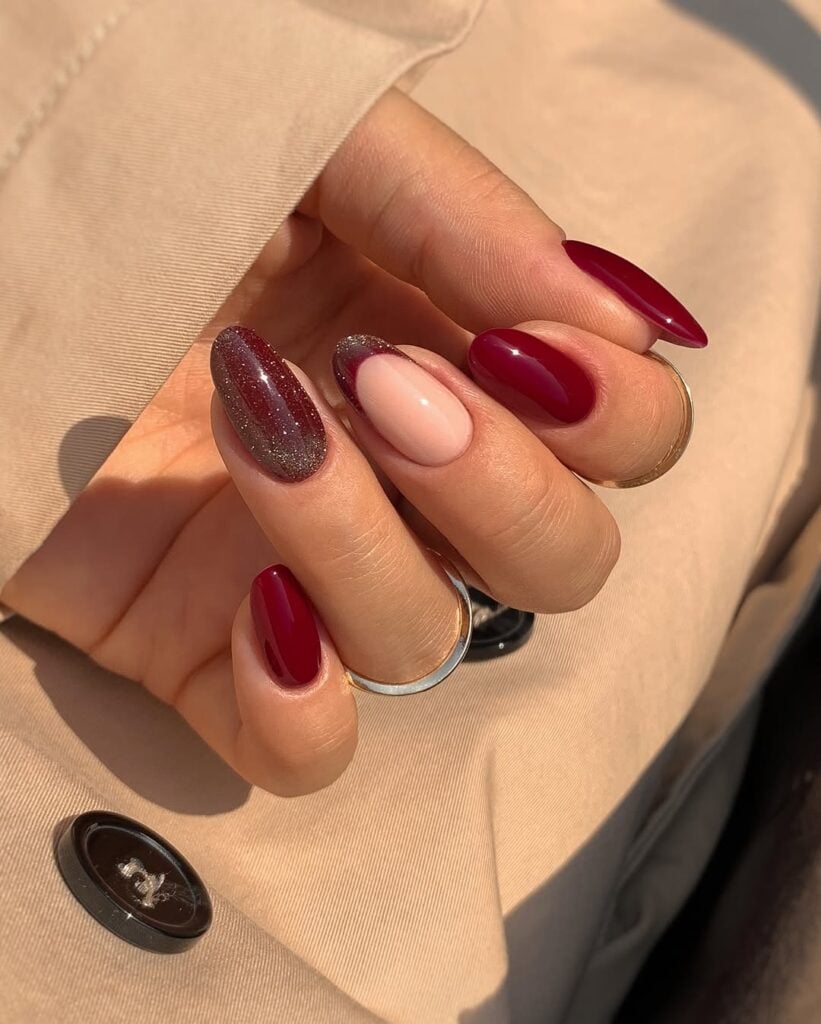 Mãos de pele clara, com anel em prata e unha amendoada vermelho vinho com glitter e francesinha 