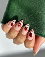 Mão de pele clara, com unha amendoada nude decorada com bota de Natal