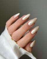 Mão de pele clara, com anéis em dourado e unha amendoada vanilla chrome